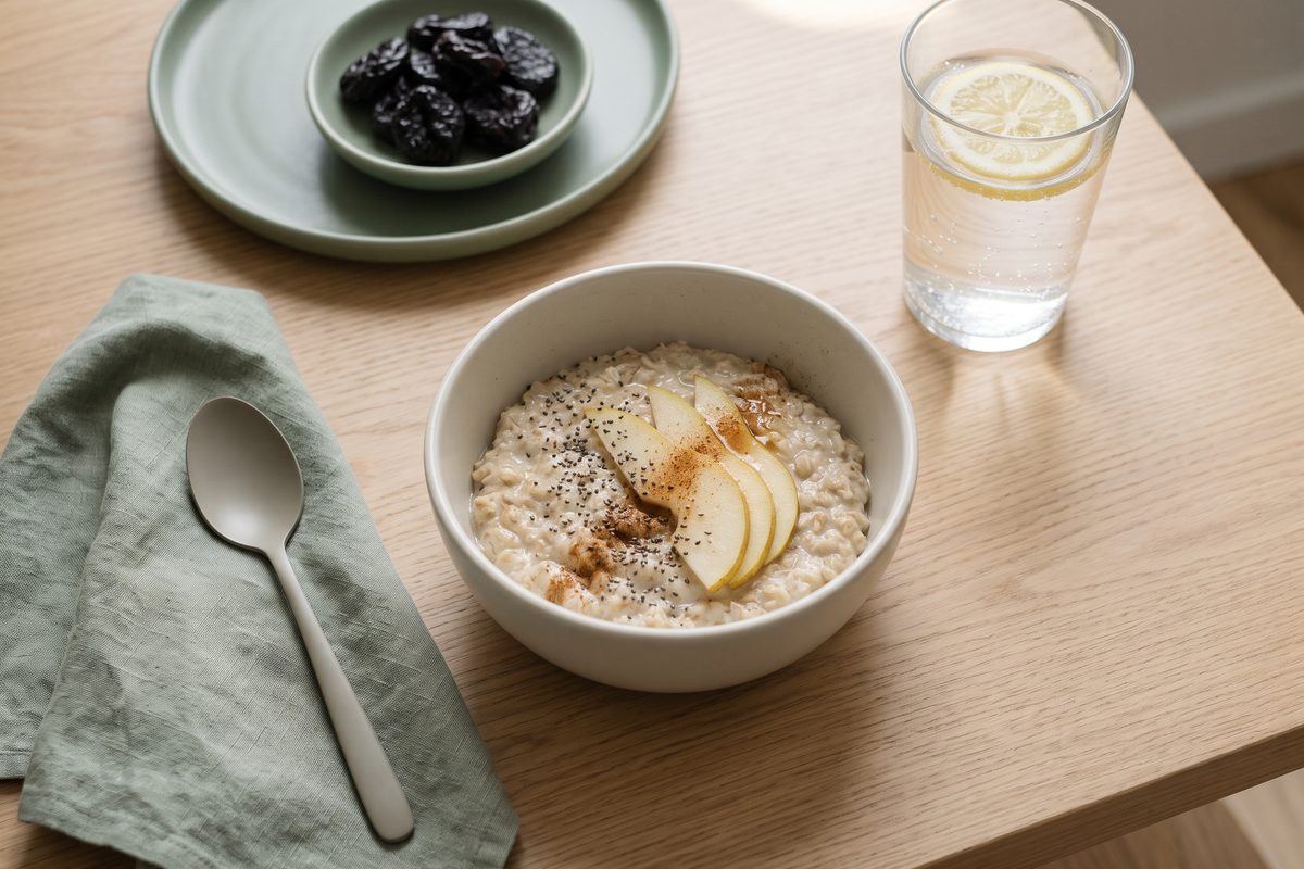 A bowl of oatmeal with pear and chia seeds, a small dish of prunes and a glass of water with lemon