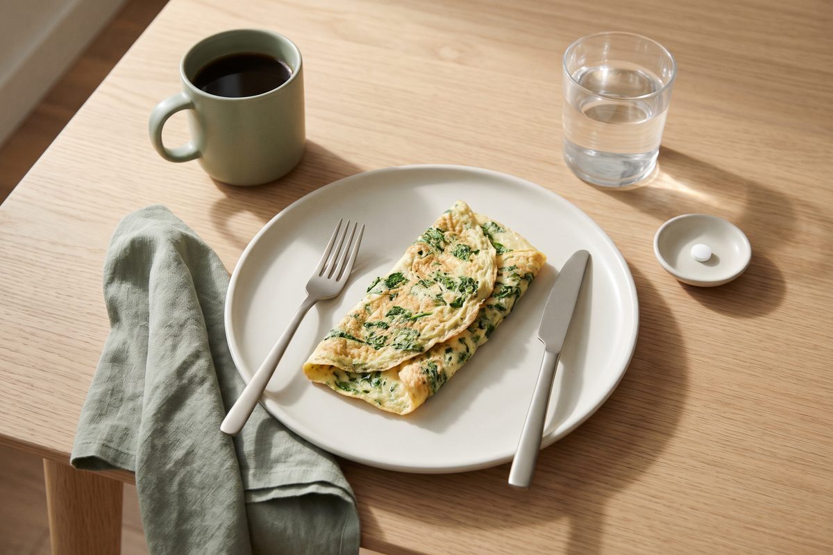 A spinach omelet, a cup of coffee, a glass of water and a plain tablet on a small dish on a breakfast table
