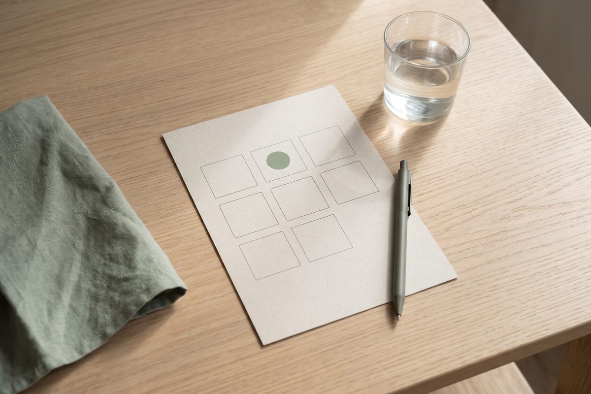 A paper weekly planner with one day marked, a pen and a glass of water on an oak table